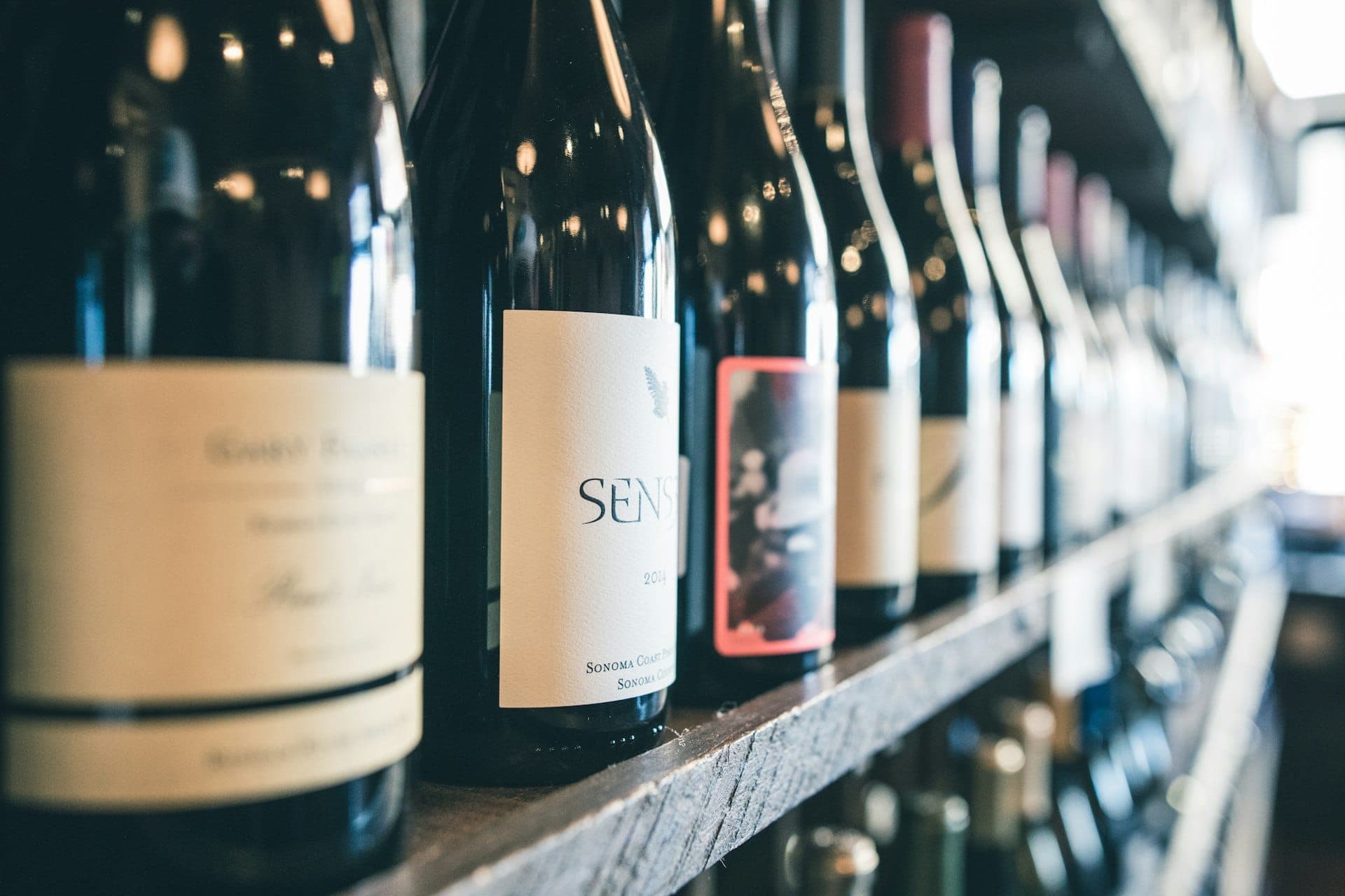 Wine bottles lined up on a shelf with warm bokeh lighting